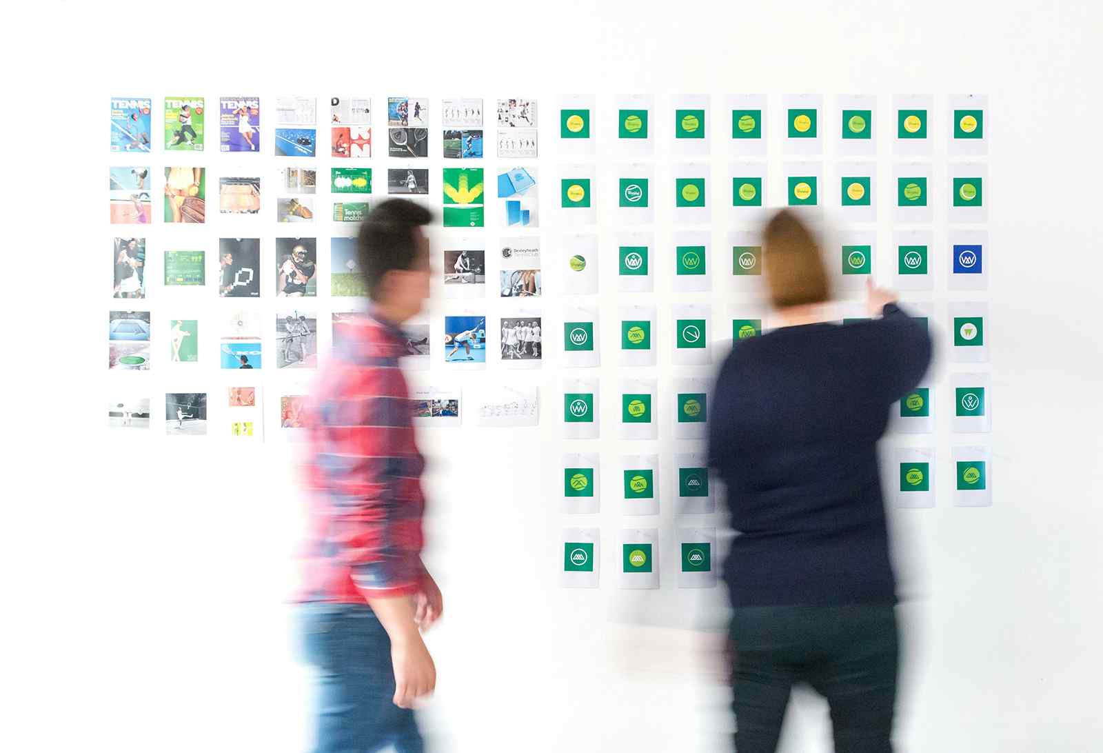 Branding agency designers collaborating on a project with logo variations and visuals displayed on the wall.