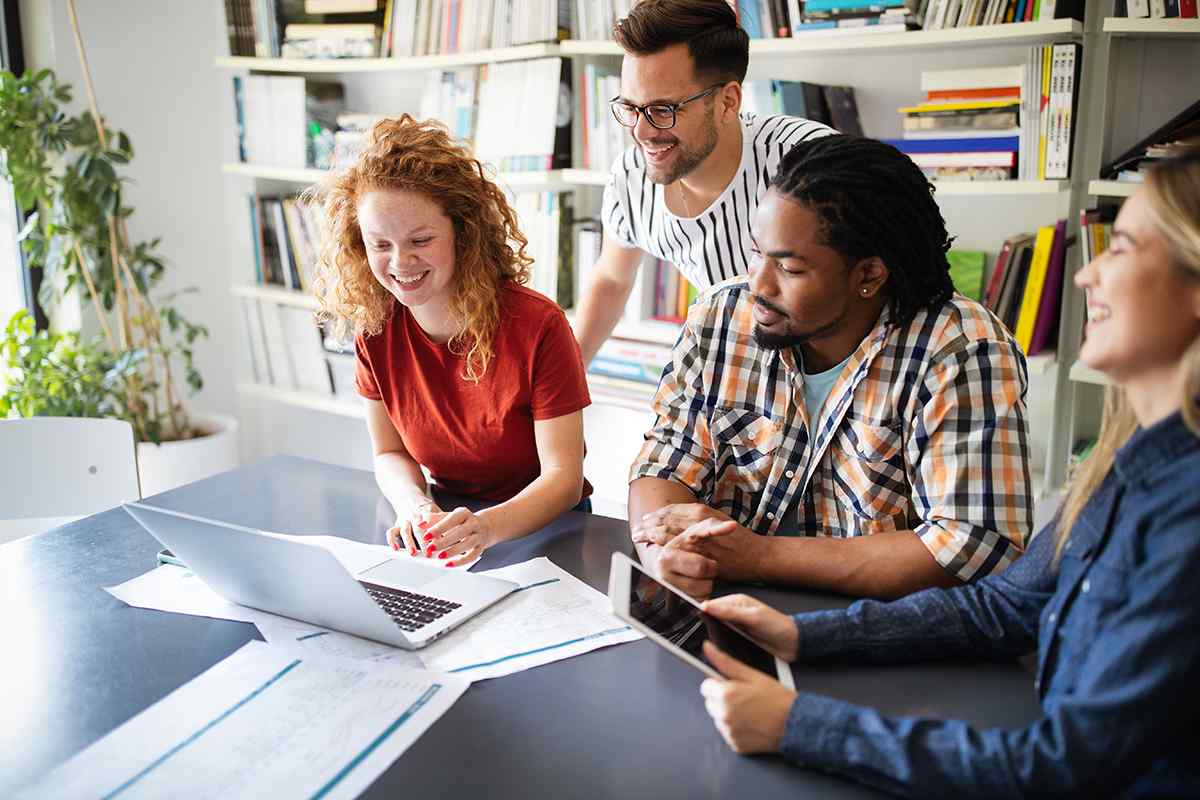 Diverse group of young marketing professionals gathered around a laptop, collecting data to create an Ideal Customer Profile (ICP) for their client