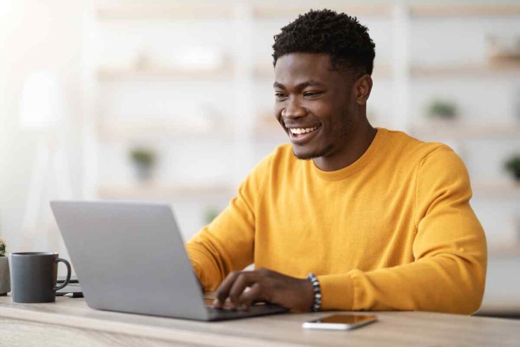 Young black businessman or indie maker working on laptop and smiling, illustrating the concept of researching and defining an ideal customer profile (ICP) for businesses