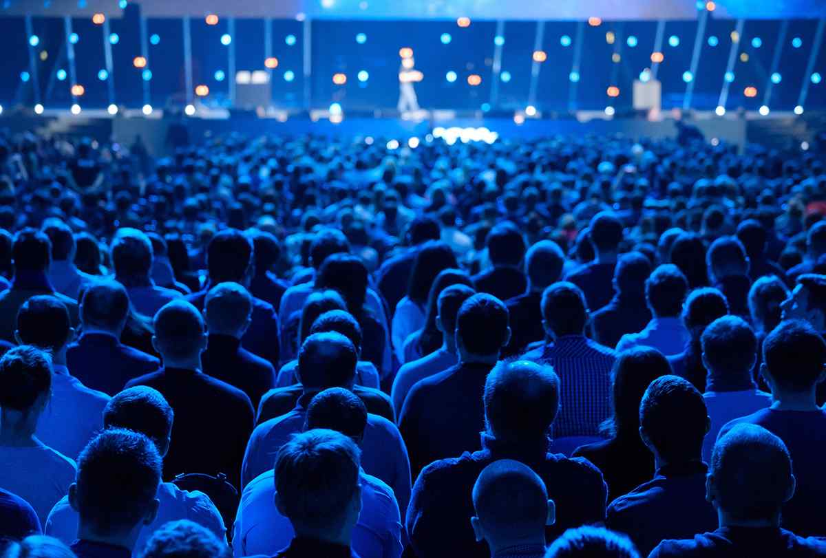 Audience seated at an event, listening to a speaker on stage, conceptualizing the implementation of an Ideal Customer Profile (ICP) into a company's marketing efforts