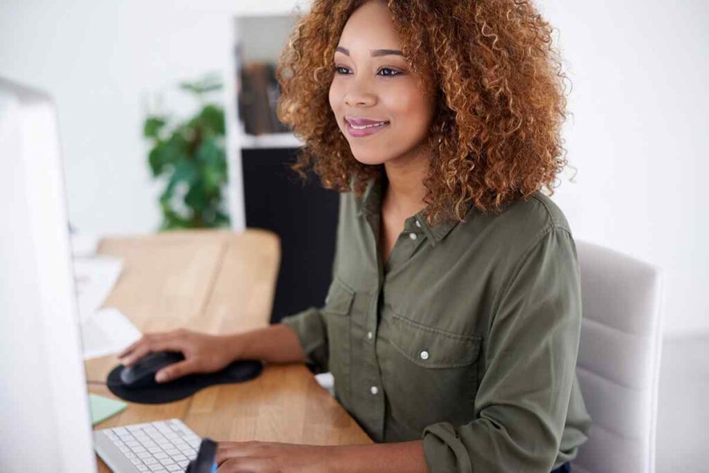 Smiling woman working on a computer in an office setting, representing sales enablement design and development.