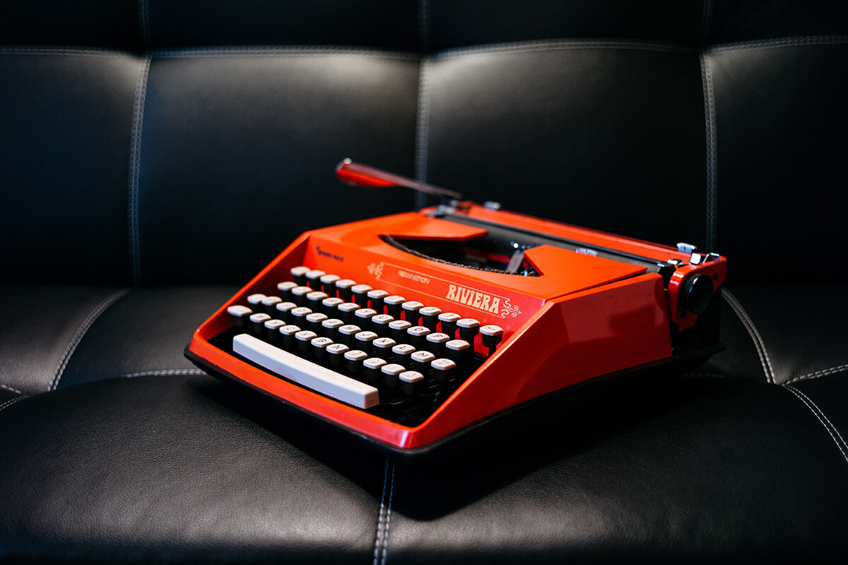 Content marketing for brand awareness using traditional methods. Red typewriter on top of black leather sofa.