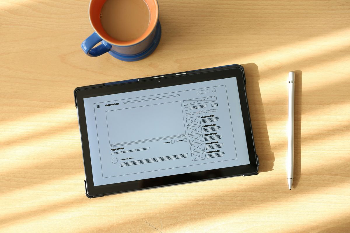 Tablet displaying a wireframe design next to a coffee cup, a crucial step in the process of designing a digital product.