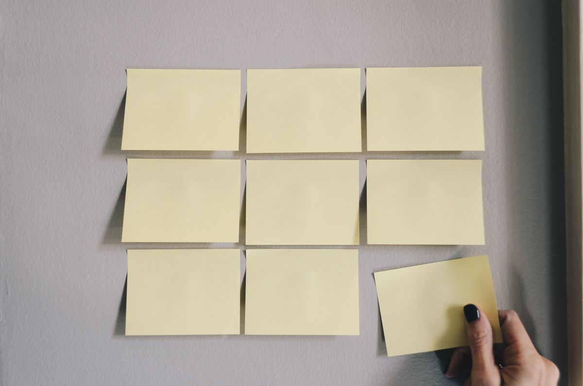 Hand placing a sticky note on a wall grid. A concept representing digital product design process and User Experience (UX) research.