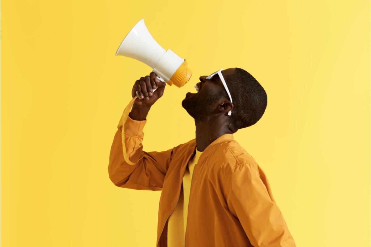 Modern, middle aged black man (back-light lit) shouting n megaphone against yellow background. A concept image for performance creative advertising - one of 10 growth marketing strategies for business success in 2025.